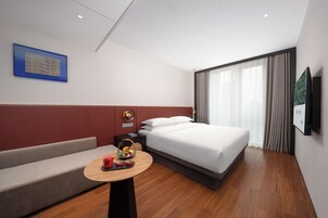 Una habitación de hotel moderna con cama, sofá, una pequeña mesa con frutero y televisor montado en la pared.