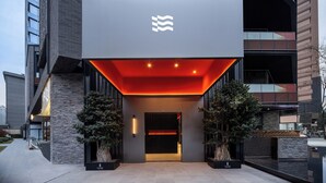 A modern building entrance with a prominent logo, a red-lit entrance canopy, and two potted trees. - SSAW Garden Hotel Chengdu - Chunxi Road Taikoo Li Branch (Chengdu)