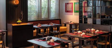 Un restaurante con varias mesas, cabinas, una barra y un amplio ventanal con persianas.
