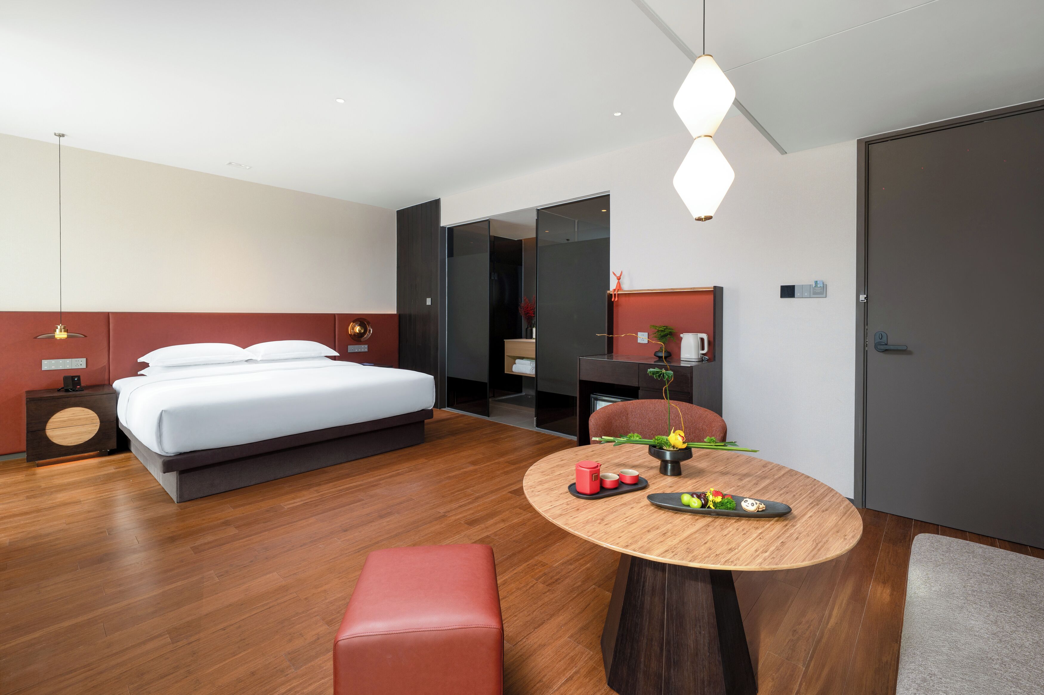 Une chambre d’hôtel moderne dotée d’un grand lit, d’une table à manger avec un banc rouge, d’un petit coin cuisine et d’une salle de bain séparée.