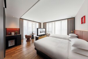 Habitación de hotel con dos camas, un televisor, un escritorio con cafetera y una mesita con una planta.