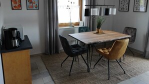 Un'area pranzo moderna con un tavolo in legno, sedie nere e marroni, una macchina da caffè e una finestra con tende.