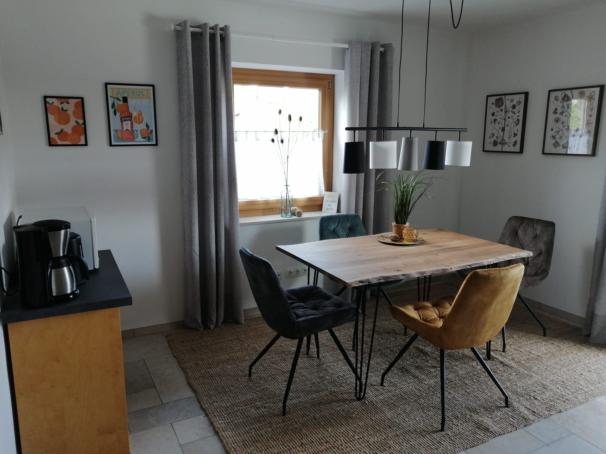 Une cuisine moderne avec une table en bois, deux chaises, une machine à café et une fenêtre avec des rideaux.