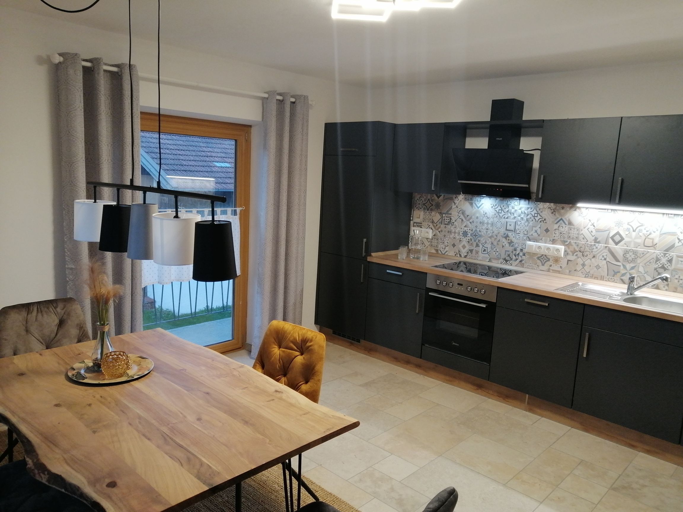 Une cuisine moderne avec des meubles de couleur sombre, un plan de travail en bois et un four encastré.