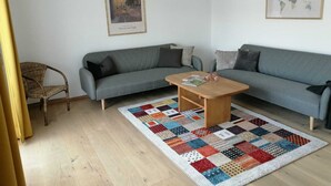 Un soggiorno con due divani grigi, un tavolino in legno, un tappeto patchwork colorato, una poltrona in vimini e due quadri appesi alle pareti.