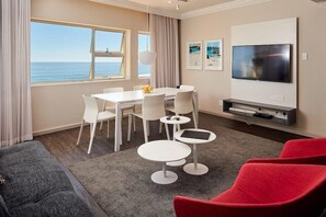 A modern living room with a dining area, a flat-screen TV, and a view of the ocean. - THE Riviera (Cape Town)