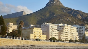A coastal cityscape with a prominent mountain in the background, featuring multi-story residential buildings with balconies and a paved walkway in the foreground. - The Riviera (Cape Town)