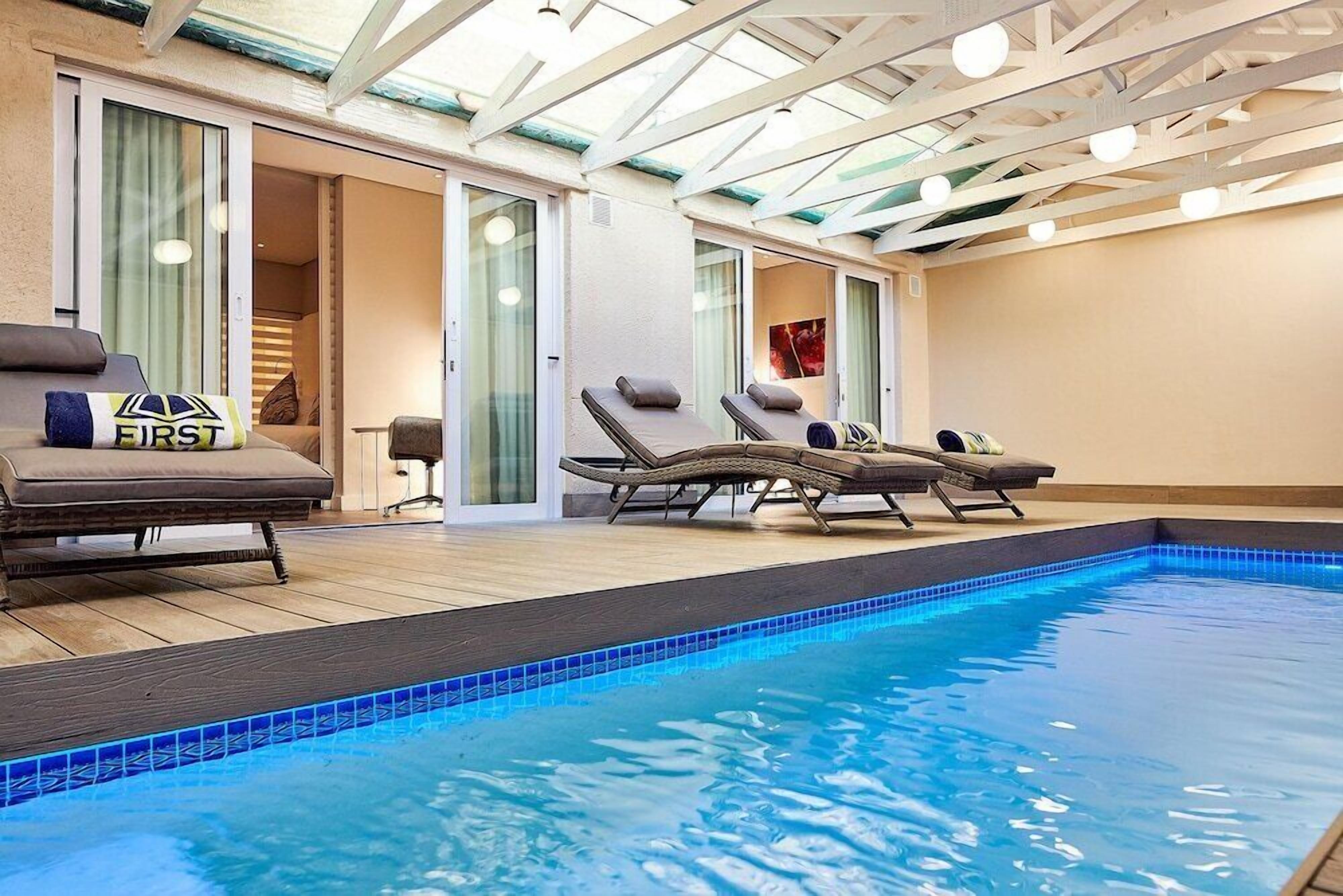 An indoor swimming pool with lounge chairs and a glass ceiling.
