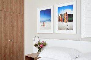 Quarto com cama, mesa de cabeceira, vaso com flores e duas molduras na parede.