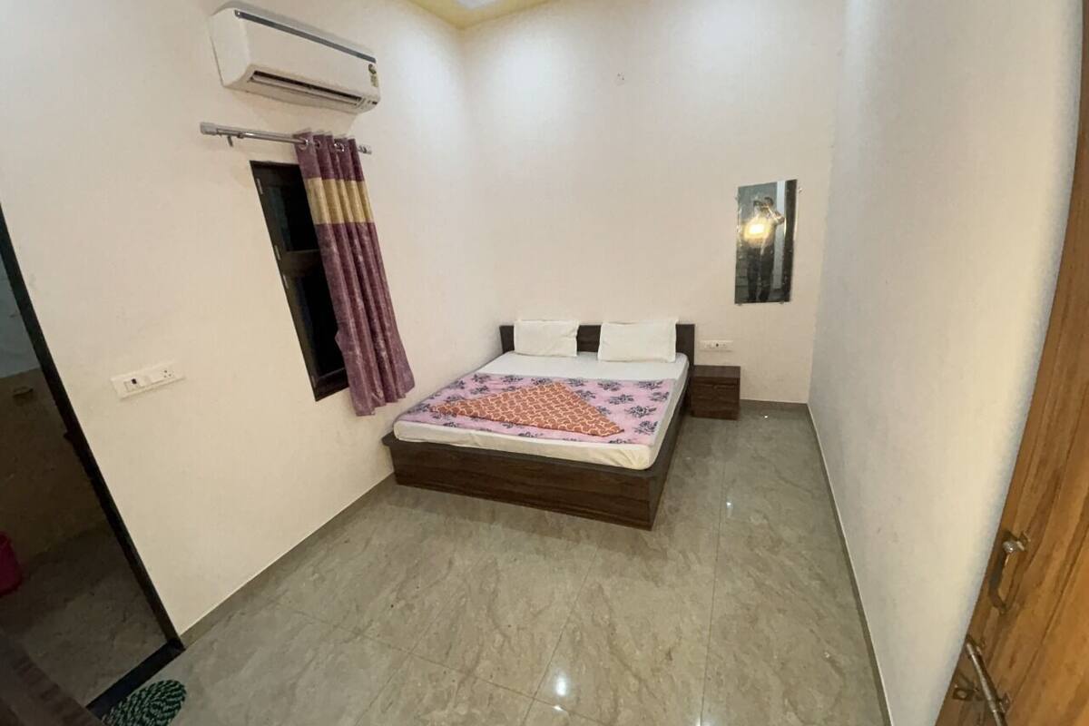 A bedroom with a bed, an air conditioning unit, a small window, and a mirror.