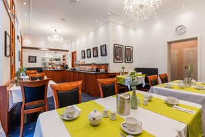 Zona pranzo dell'hotel con tavoli apparecchiati per la colazione, un bar e opere d'arte alle pareti.