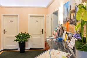 A hotel reception area with two doors, a potted plant, and a counter with brochures and a map.