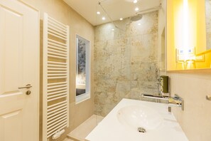 Un baño moderno con un lavabo blanco grande, ducha con puerta de cristal y un perchero para toallas.