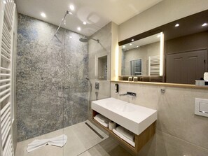 Un baño moderno con un espejo grande, ducha y tocador con lavamanos.
