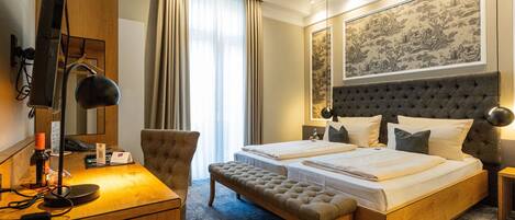 Une chambre d’hôtel comprenant un lit, un bureau, une chaise, un banc et une grande œuvre d’art encadrée accrochée au mur.