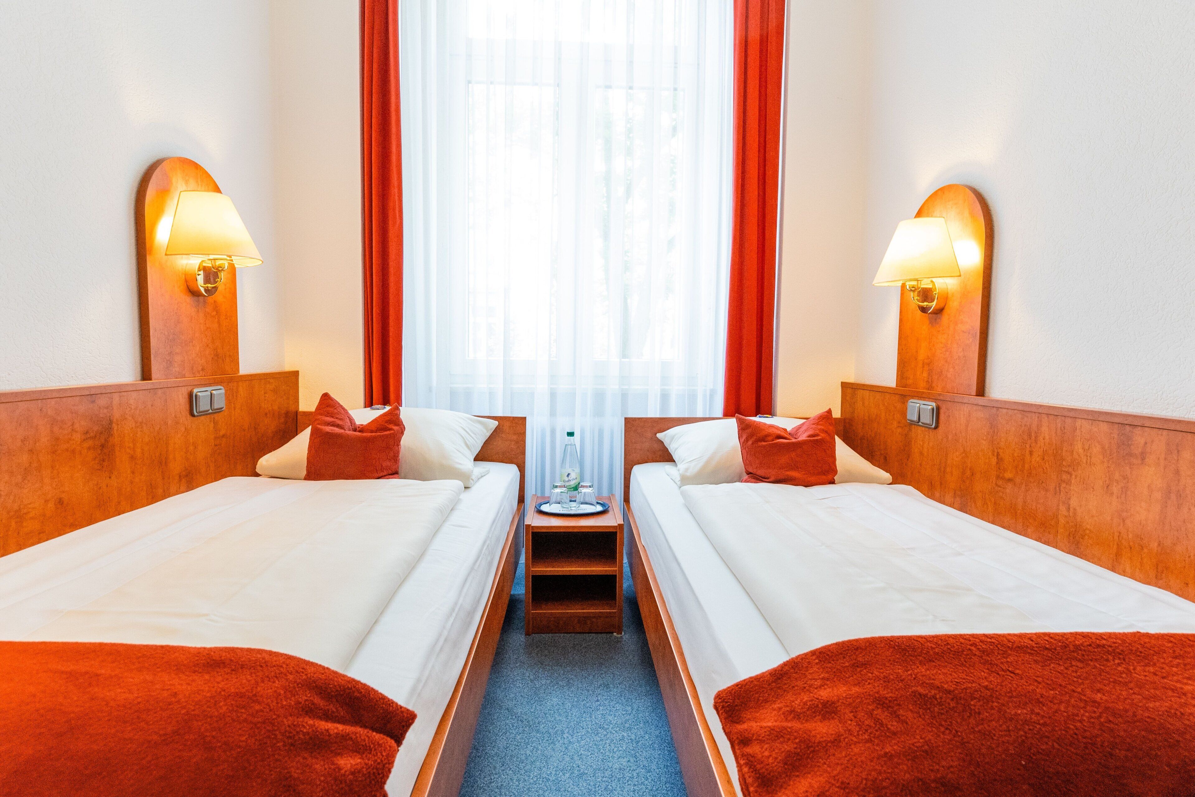 Una camera d'albergo con due letti, un tavolino e una finestra con tende.