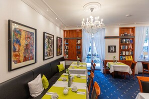 A dining area with tables set for service, a seating area with a sofa, and a view through a window.