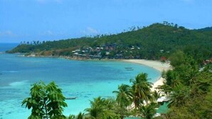 Un complejo turístico costero con una playa de arena, aguas turquesas cristalinas y abundante vegetación.