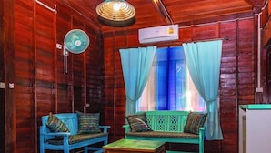 Une pièce aux murs en bois, avec un ventilateur de plafond, un appareil de climatisation, une fenêtre ornée de rideaux bleus et deux canapés bleus agrémentés de coussins à motifs.
