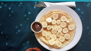 Un plato de tortitas cubiertas con rodajas de plátano y un cuenco pequeño de salsa de chocolate, sobre una mesa con mantel oscuro.