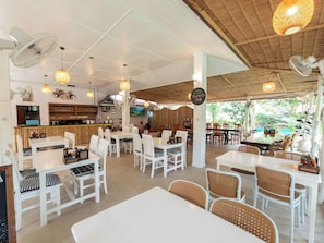 A restaurant with white tables and chairs, a bar area, and a view of greenery outside. - Baan Haad Yao Villas (Ko Pha-ngan)