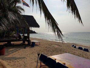 Uma praia com uma cabana de palha, cadeiras de praia e uma bandeira.