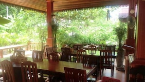 Un espace de restauration intérieur avec des tables et des chaises en bois, entouré d’une végétation luxuriante que l’on peut admirer à travers de grandes fenêtres.