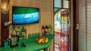 Una cocina con encimera verde, cafetera, frutero y televisor mostrando un pronóstico del tiempo.