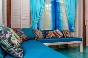 Um sofá azul com almofadas coloridas, um banco branco e cortinas azuis.