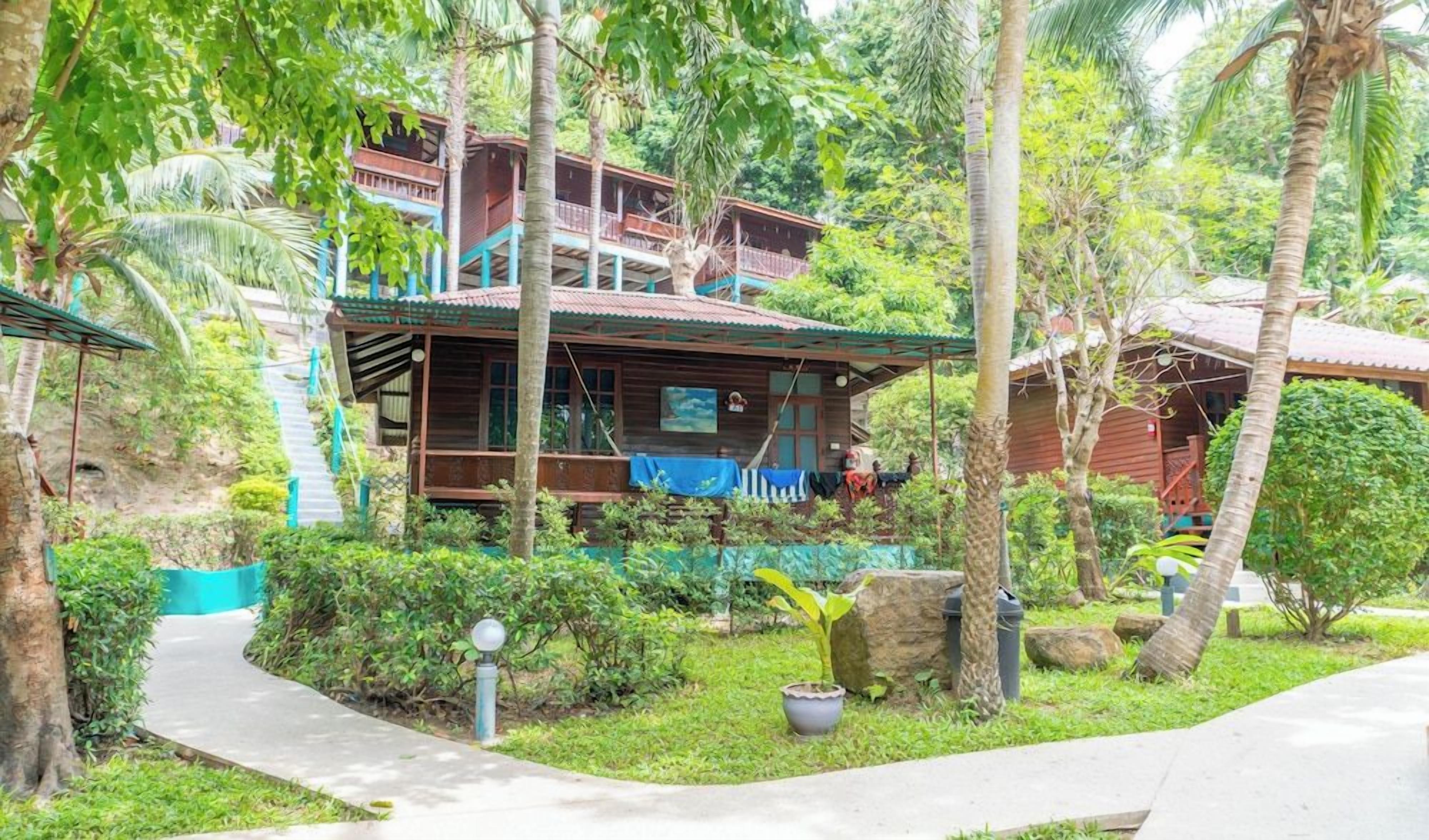 A wooden building with multiple balconies, surrounded by lush greenery and a pathway.