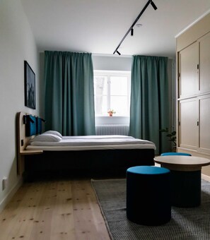 A bedroom with a bed, a window, curtains, a radiator, a bedside table, and a small round table. - Stf Af Chapman Hostel (Stockholm)