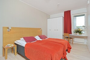 Un dormitorio con cama, escritorio, silla, armario y ventana con cortinas.