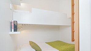 A bunk bed with a white headboard, a shelf with books, a green pillow, and a green blanket. - Forenom City Suites Tampere (Tampere)