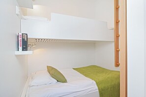 Una cama individual con dos literas, cabecera blanca, un estante con libros, almohada verde y manta verde.