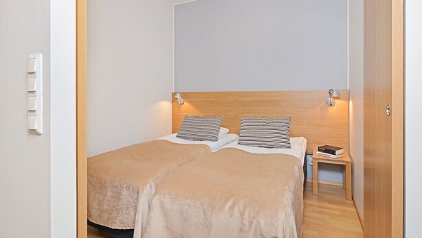 A bedroom with a bed, two bedside lamps, a nightstand, and a wall-mounted light switch. - Forenom City Suites Tampere (Tampere)