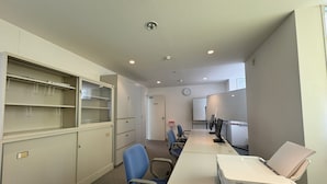 Ein Konferenzraum mit langem Tisch, Stühlen, einer Whiteboard und einer Uhr an der Wand.