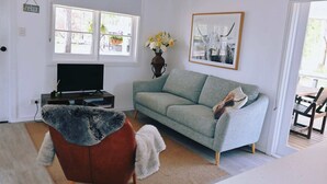 A living room with a grey sofa, a television on a stand, a vase with flowers, and a framed picture on the wall.