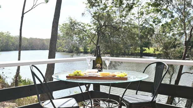 Una mesa con una botella de vino, copas y una bandeja de queso, con vistas a un lago.