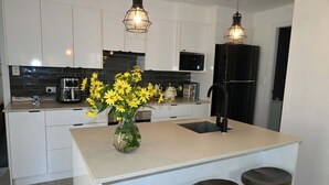 Una cocina moderna con armarios blancos, un salpicadero negro y una isla central con taburetes.