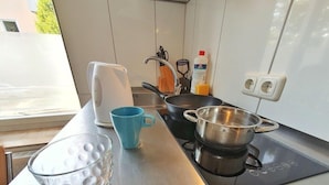 A kitchen with a stove, a kettle, a blue mug, and a glass. - B & L Hostel (Bremen)