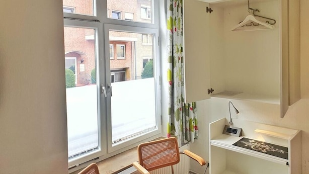 A room with a large window, a chair, a radiator, a desk with a lamp, and a hanging coat rack. - B & L Hostel (Bremen)