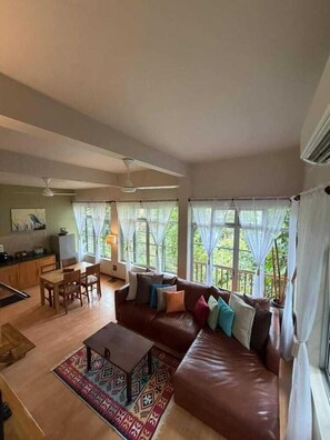 A spacious living area with a brown leather sofa, a dining table with chairs, and a kitchen area in the background. - Ambong-ambong Langkawi Rainforest Retreat (Langkawi)