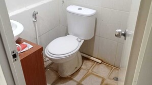 A small, basic bathroom with a toilet, a sink, and a wooden cabinet. - Japlen Room (South Tangerang)