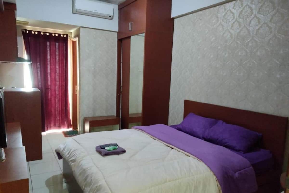 A bedroom with a bed, a nightstand, a mirror, and a window with curtains.