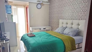 A bedroom with a bed, a desk, a chair, a clock, and a water dispenser. - Japlen Room (South Tangerang)