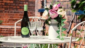 Una mesa metálica redonda con una botella de vino y dos copas, rodeada de sillas metálicas blancas.