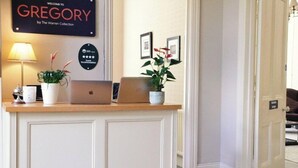 Un mostrador de recepción con una computadora portátil, una planta y un cartel de bienvenida para Gregory, cortesía de The Warren Collection.