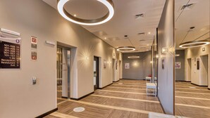Un couloir d’hôtel avec un comptoir d’accueil, des ascenseurs et un mur recouvert de miroirs.
