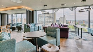 Un espace de détente moderne, doté de sièges, de tables et de grandes fenêtres offrant une vue sur la ville.