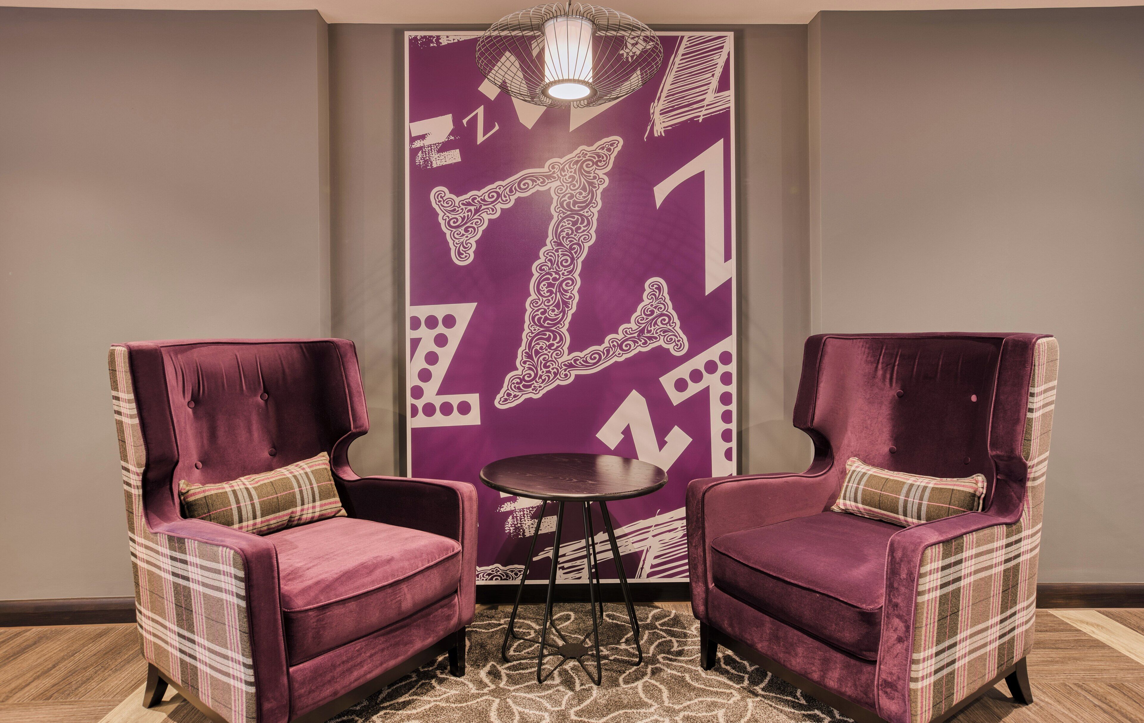 A room with two plush armchairs, a small round table, and a wall with a geometric pattern.